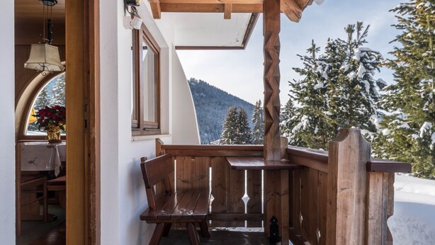 Un banco de madera y una mesa frente a un edificio, con vista a árboles nevados y montañas.