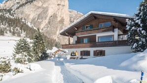 Un chalet de dos pisos con balcón, rodeado de montañas nevadas.