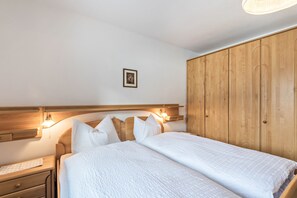 Een tweepersoonsbed met een houten hoofdbord, bedlampjes en een houten garderobe.