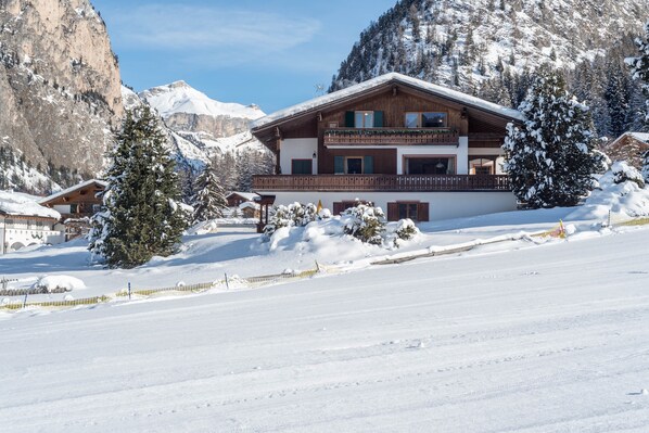 Un hotel de estilo chalet con fachada de madera, varios balcones y un paisaje nevado con montañas al fondo.
