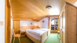 A wooden-paneled bedroom with a bed, bedside tables, a chair, and a door leading to a balcony.