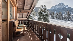 A wooden balcony with a bench, a wooden railing, and a view of snow-covered mountains.
