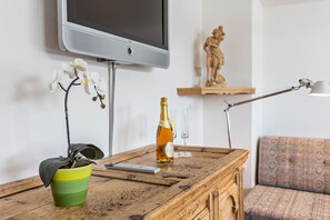 A wooden table with a remote control, a bottle of champagne, and a potted orchid.