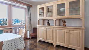 A room with a view of mountains, a dining table with a polka dot tablecloth, a wooden cabinet with glass doors, and a wicker chair.