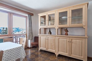 A room with a view of mountains, a dining table with a polka dot tablecloth, a wooden cabinet with glass doors, and a wicker chair.