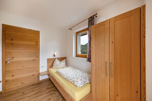 Un dormitorio con cama de madera, ventana con cortinas, armario de madera y una puerta.