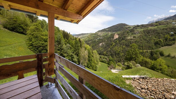 Um deck de madeira com vista para um vale verde e montanhas.