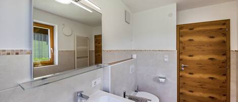 Un baño con estante de vidrio, lavamanos, inodoro y puerta de madera.