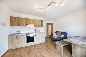 Una cucina compatta con mobili in legno, forno integrato, lavello e zona pranzo con tavolo e panchina.