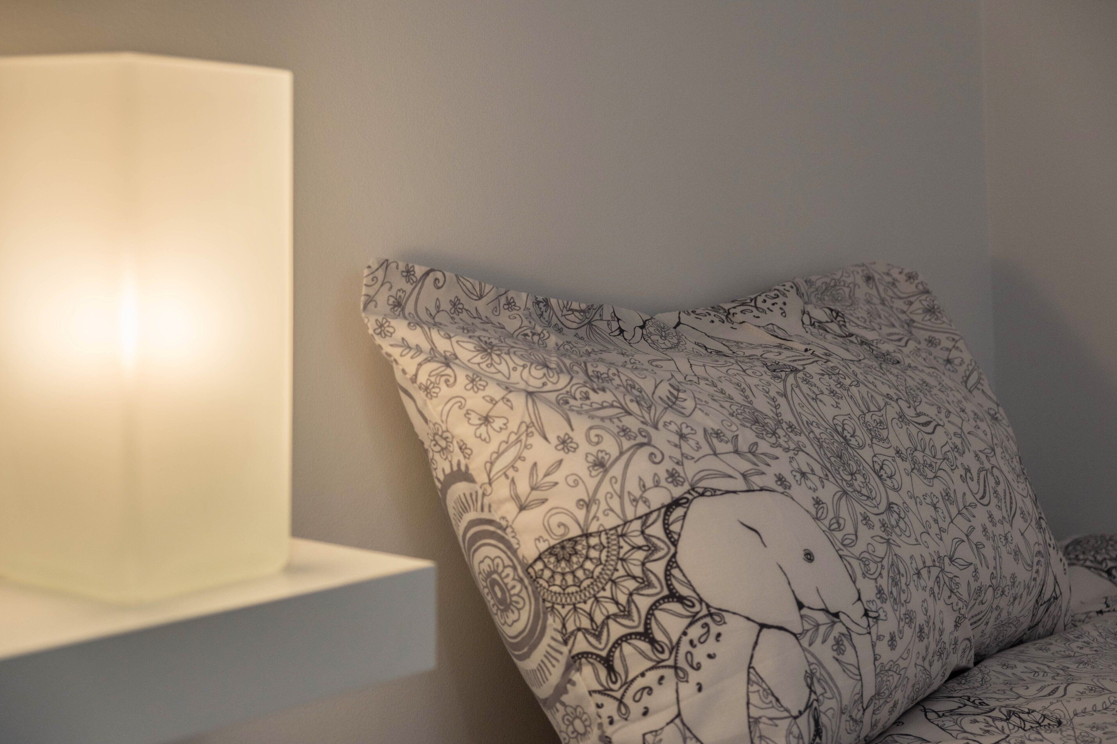 A bed with a patterned pillow and a bedside lamp.