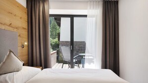 Un dormitorio con una cama, cabecera de madera, ventana con cortinas y vistas a un patio exterior.