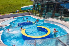 Una piscina con múltiples carriles, un tobogán acuático y un edificio de cristal al fondo.