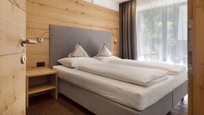 Una cama doble con cabecera gris, una mesita de noche de madera y una ventana con cortinas de gasa.