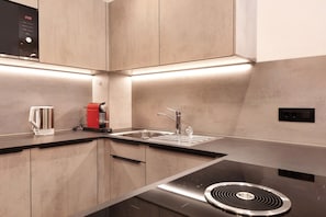 A modern kitchen with a stainless steel sink, a kettle, and a red appliance, likely a coffee maker.