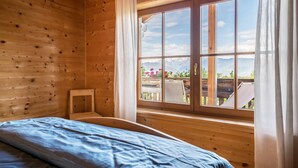 Una habitación de cabaña de madera con cama, ventana con cortinas y vistas a las montañas.