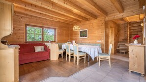 Interior de una cabaña de madera con una mesa de comedor, sillas, un sofá y una escalera.
