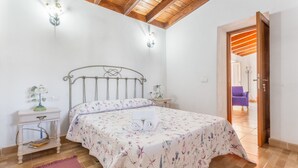 Une chambre à coucher comprenant un lit, des tables de chevet, une commode, un plafond en bois et une porte donnant sur une autre pièce.