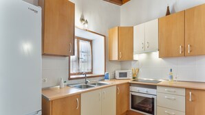 Une cuisine avec des meubles de rangement en bois, un réfrigérateur blanc, un four à micro-ondes, un évier et une fenêtre avec des rideaux.