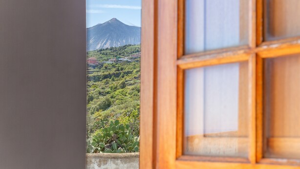 Une vue à travers une fenêtre avec un cadre en bois, une montagne et de la verdure.