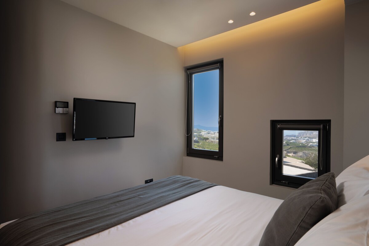 Un dormitorio moderno con cama, televisor montado y ventana con vistas.