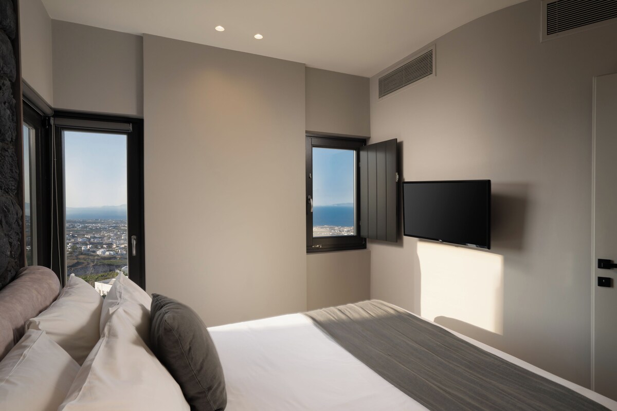 Una habitación de hotel moderna con una cama grande, un televisor montado en la pared y un ventanal con vistas a la ciudad.