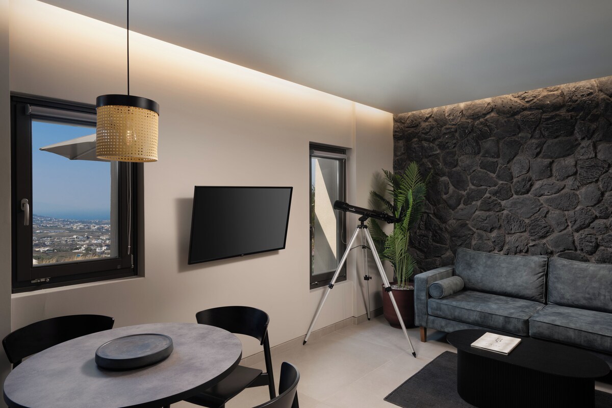 Una sala de estar moderna con una pared de piedra, un televisor montado, un telescopio y una zona de comedor con sillas y una mesa.