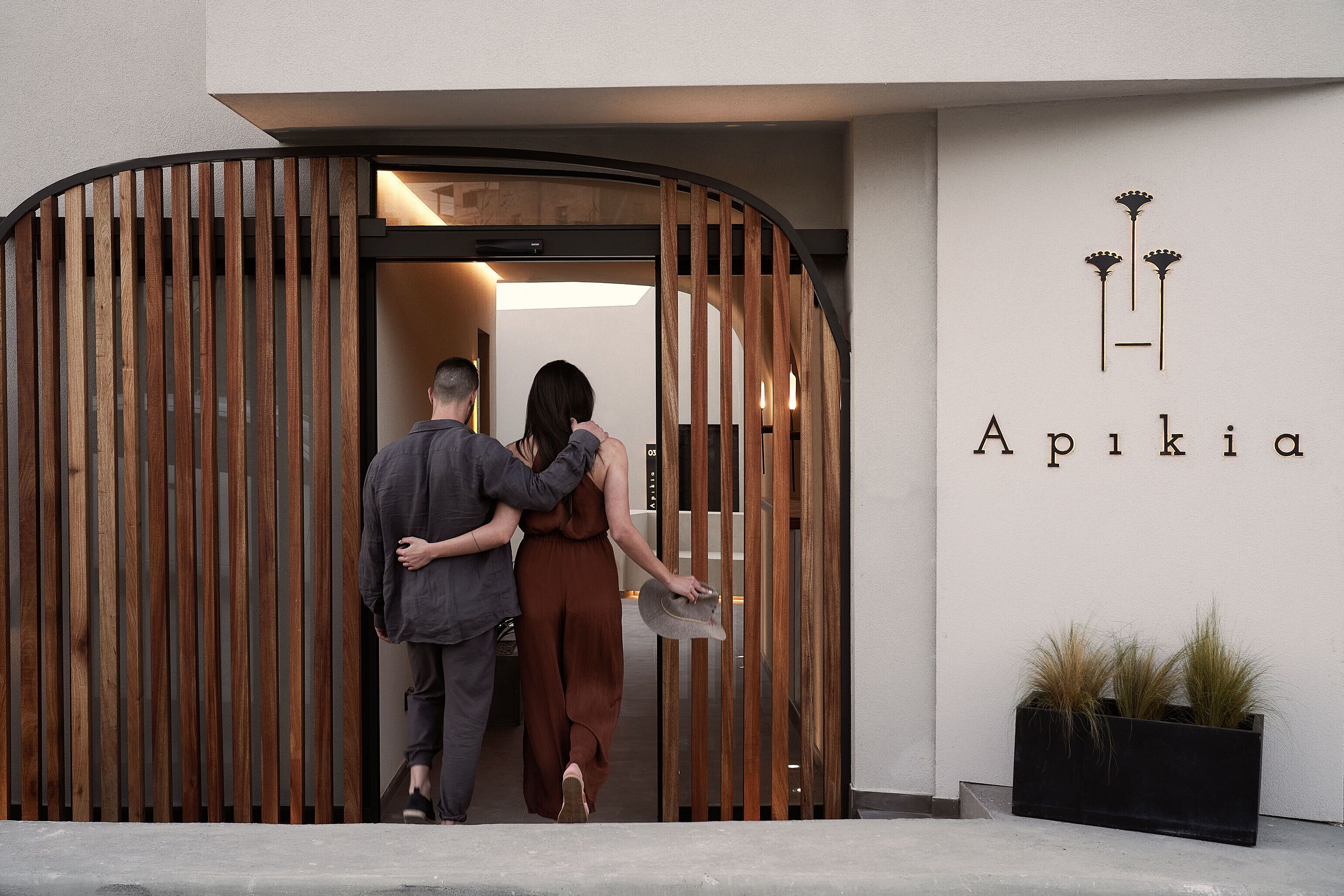 Un couple sort d’un bâtiment à la façade en bois, sur lequel on peut lire l’inscription « Apikia ».