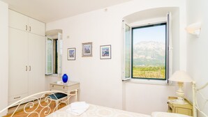 A bedroom with a bed, a dresser, a vanity, and a window with a mountain view. - Stone House Dimato (Konavle)