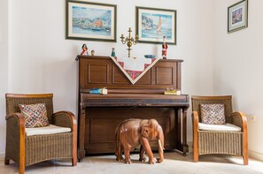 A room with a piano, two wicker chairs with patterned cushions, a small elephant figurine, and three framed paintings on the wall. - Stone House Dimato (Konavle)