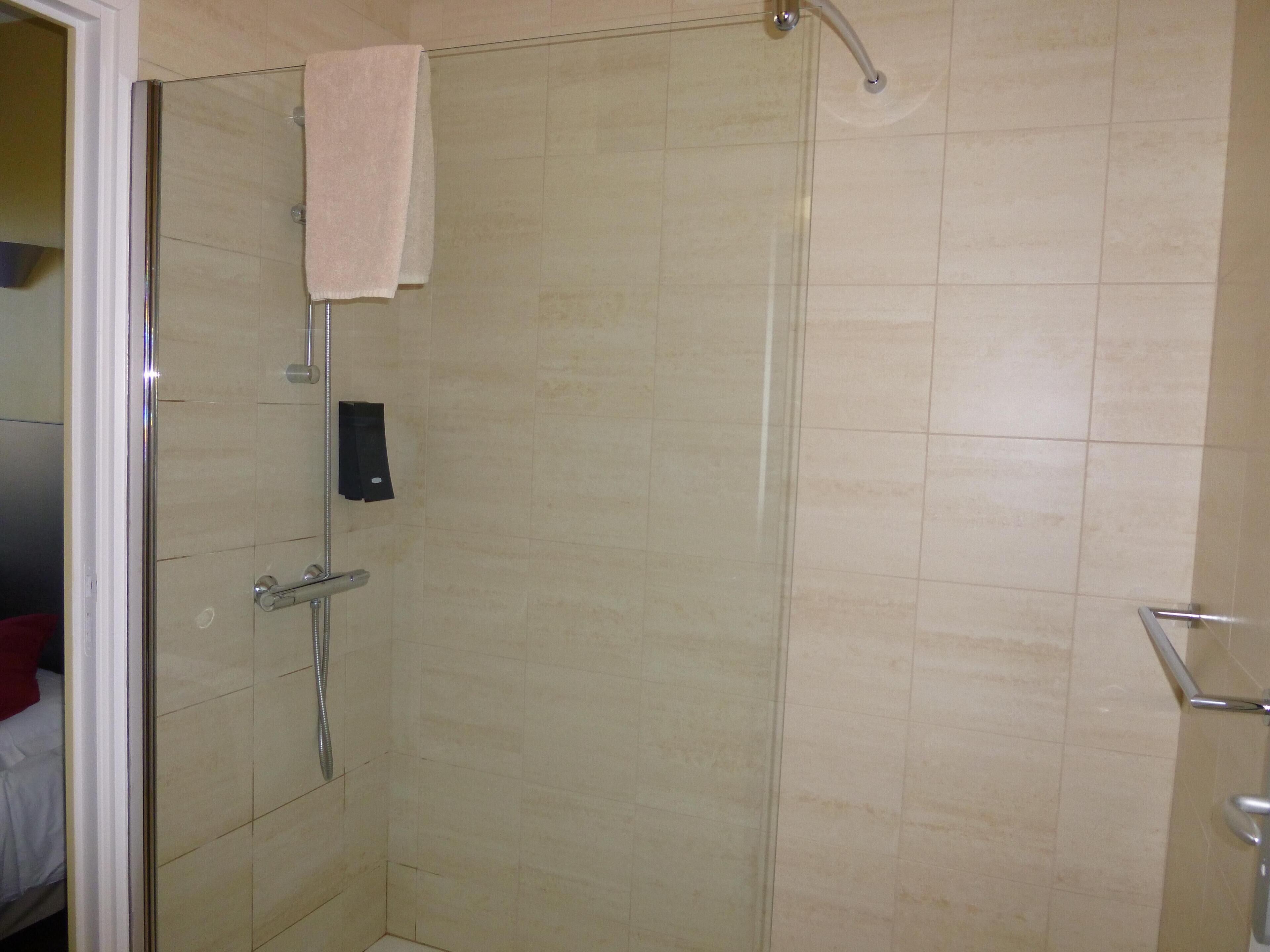 A shower with a glass door, a towel hanging on the door, and a soap dispenser mounted on the wall.