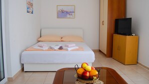 A neatly arranged bedroom with a bed, a wooden wardrobe, a television on a stand, and a fruit basket on a table. - Apartment Lili (Supetar)