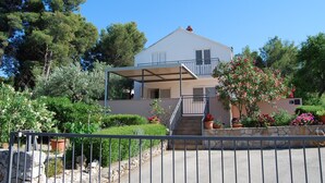 A two-story house with a covered balcony, stone steps, and a garden with various plants and flowers. - Apartment Lili (Supetar)