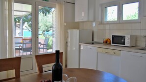 A kitchen with white cabinets, a microwave, and a refrigerator. There is a dining table with chairs and a bottle of wine. - Apartment Lili (Supetar)