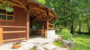 Una cabaña de madera con un porche cubierto, escalones de piedra y un jardín con macetas y flores.