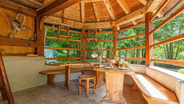 Una cabaña de madera con un ventanal grande, una banca y una mesa con varios objetos.