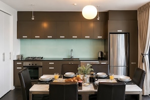 Une cuisine moderne avec des meubles de couleur sombre, un réfrigérateur en acier inoxydable et un coin repas aménagé pour le petit-déjeuner.