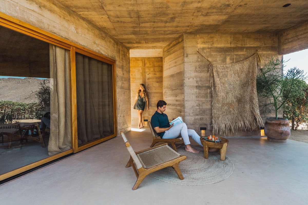 Un área de estar al aire libre moderna con un muro de concreto, un tapiz tejido y una planta en maceta.