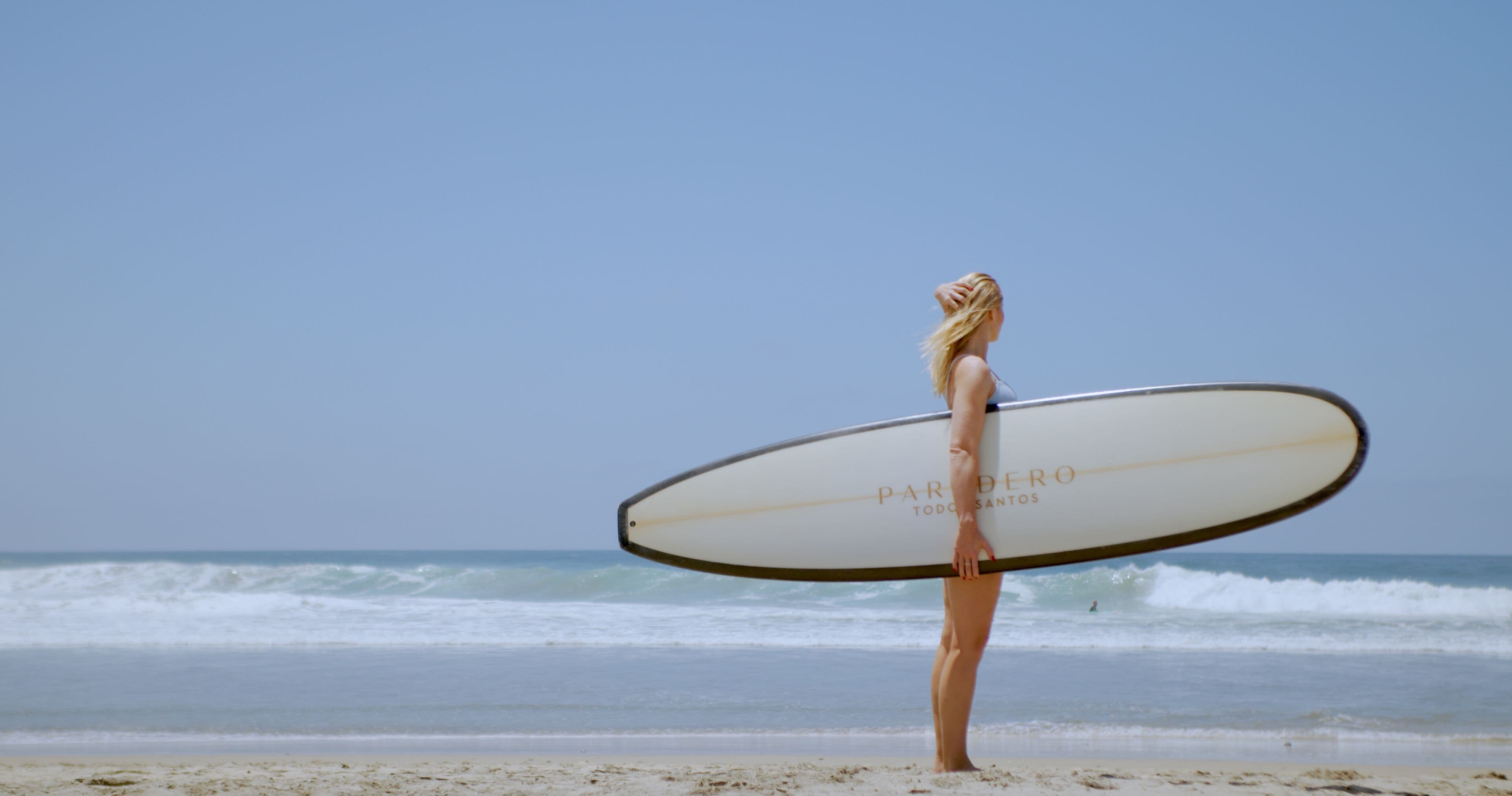 A person holding a surfboard on a beach with waves in the background.