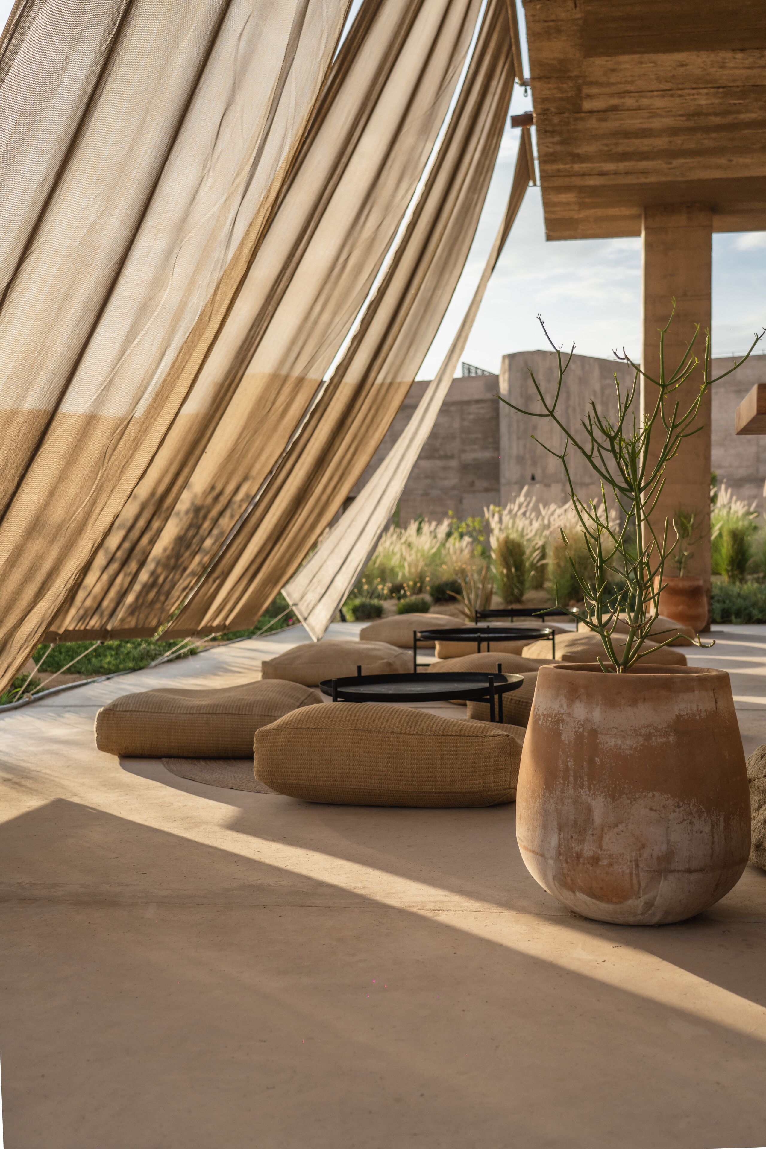 Un área de estar moderna al aire libre con una estructura metálica abstracta de gran tamaño, asientos acolchados y una planta en maceta.