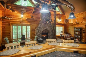A log cabin interior with a stone fireplace, wooden furniture, and hanging light fixtures. - Iron Mountain Lodge 3 Bedroom Cabin by RedAwning (Butler)