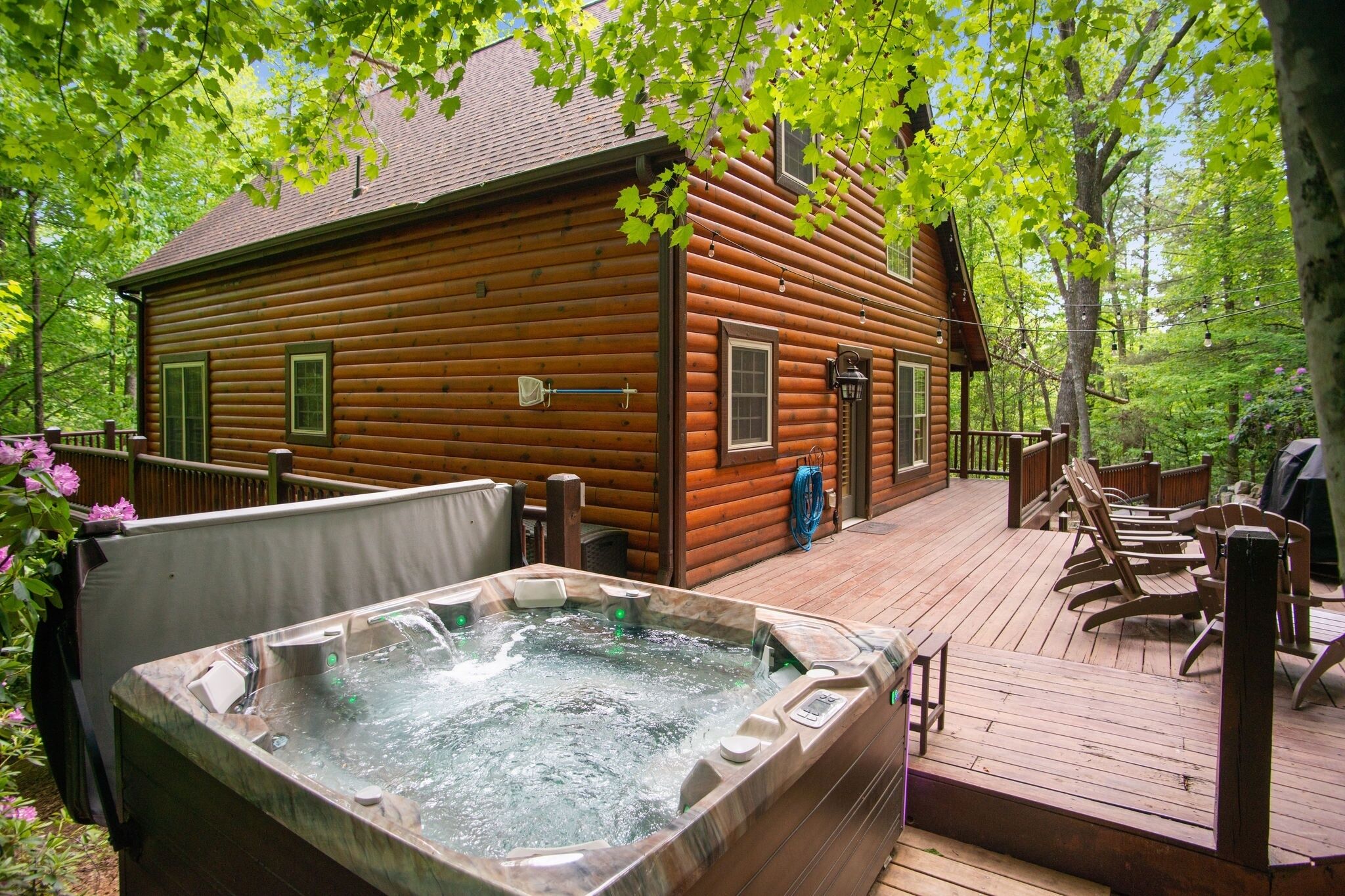 A wooden cabin with a hot tub on a deck, surrounded by trees.