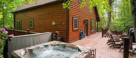 A wooden cabin with a hot tub on a deck, surrounded by trees.