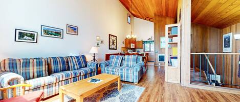 A cozy living room with a sofa, a coffee table, and a dining area with a kitchen in the background.