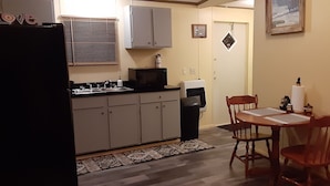 Una cocina compacta con refrigerador, microondas, lavabo y alacenas. Hay una mesa de comedor con sillas y un tapete en el piso.