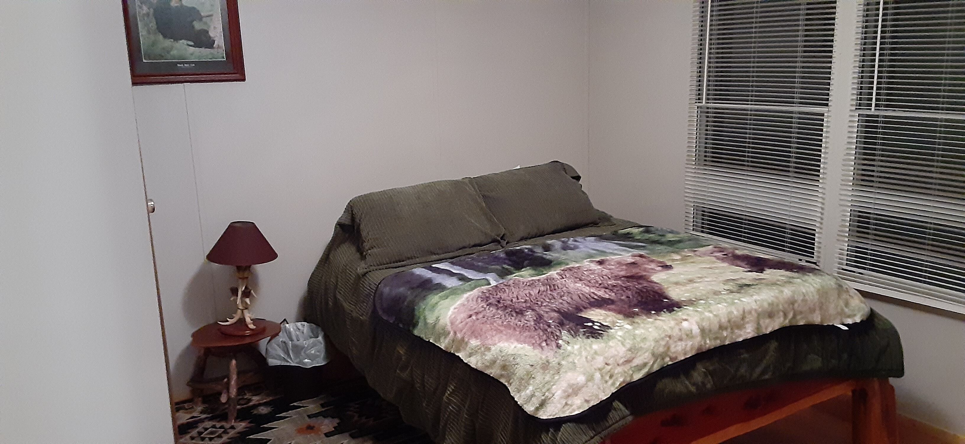 Un dormitorio pequeño con cama, mesita de noche, lámpara y ventana con persianas.
