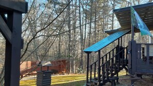 Una cabaña rústica con terraza de madera y porche cubierto, rodeada de un bosque.