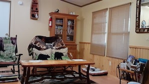 Una habitación acogedora con una mesa de madera, sillas, una estantería y una ventana con persianas.