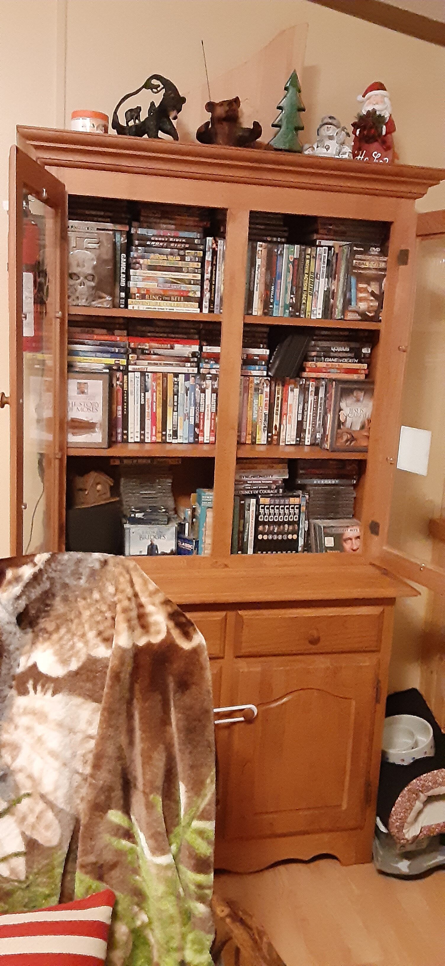 A wooden bookshelf filled with DVDs and books, a small Christmas tree, and a Santa Claus figurine.