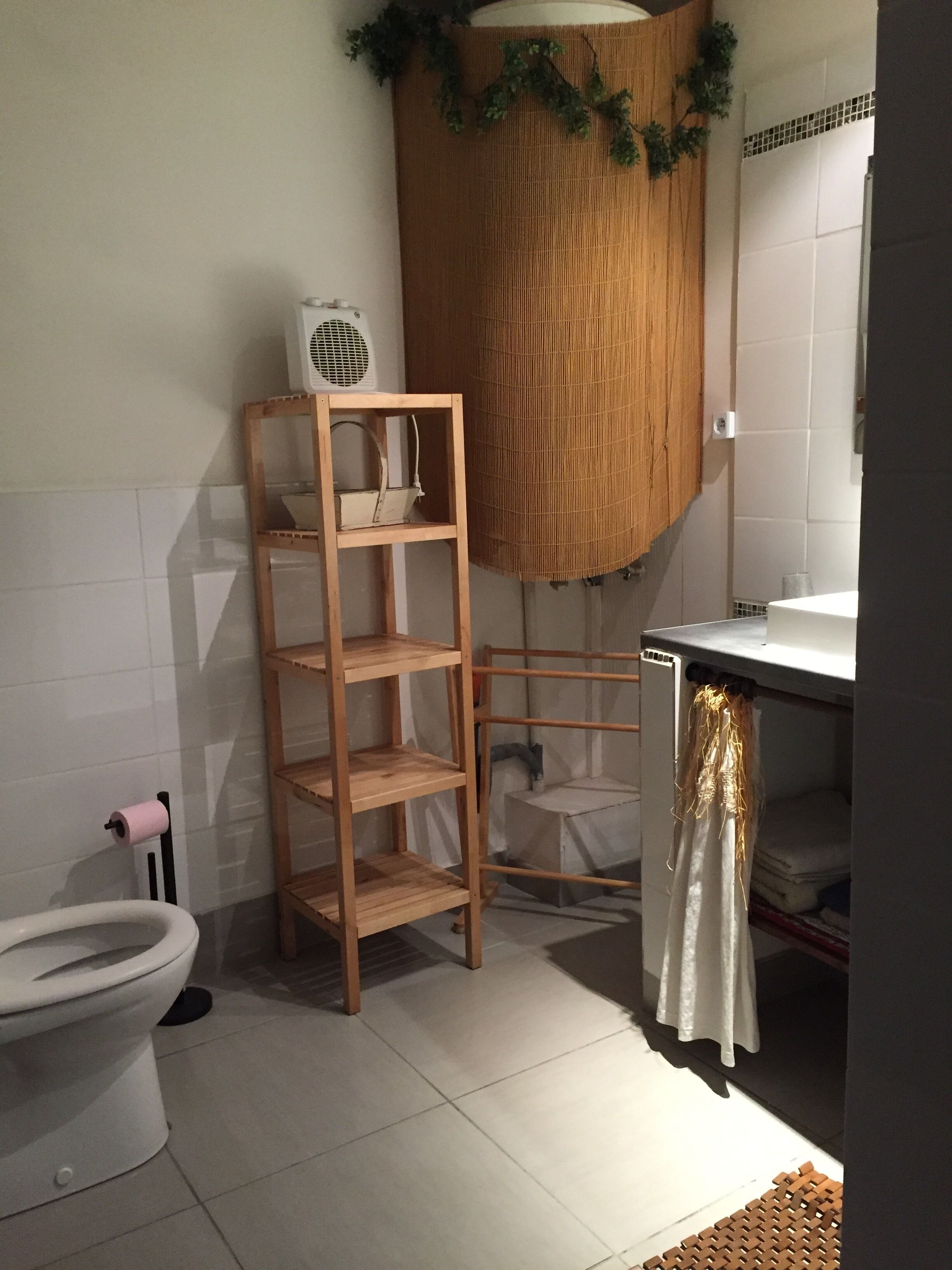 A bathroom with a toilet, a wooden shelf unit, a white sink, and a shower area.