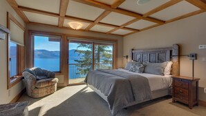 A bedroom with a large bed, a nightstand, a chair, and a view of a lake. - Gonowabie Lodge - Crystal Bay Lakefront - TLUXP (Crystal Bay)